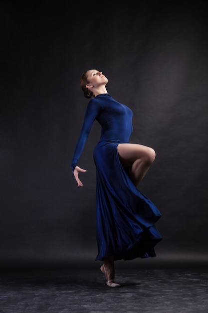 Jeune belle danseuse de ballet en longue robe bleue posant sur fond de studio
