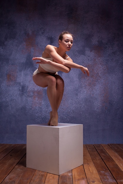 Jeune Belle Danseuse En Maillot De Bain Beige Posant Sur Cube Blanc Sur Lilas