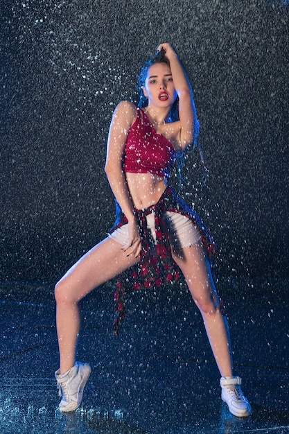 La jeune belle danseuse moderne dansant sous les gouttes d'eau dans le studio bleu aqua