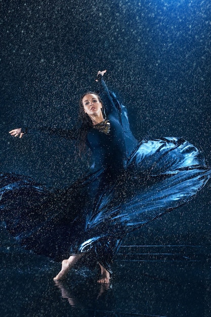 La jeune belle danseuse moderne en robe longue danse sous des gouttes d'eau dans un studio bleu aqua