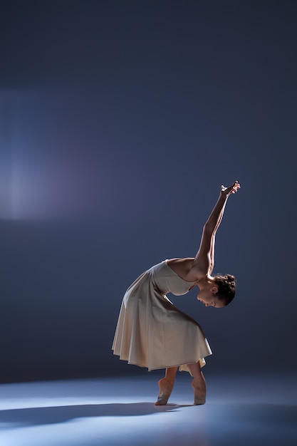 Jeune belle danseuse en robe beige dansant sur fond gris studio