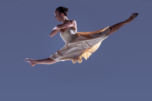Photo jeune belle danseuse en robe beige sautant sur fond gris studio