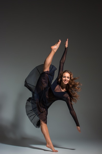 Jeune belle danseuse en robe noire posant sur un fond de studio gris foncé. Moderne, Contemporain, improvisation
