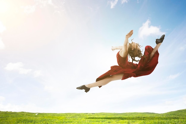 Photo jeune et belle danseuse en robe rouge sautant dans le ciel. technique mixte