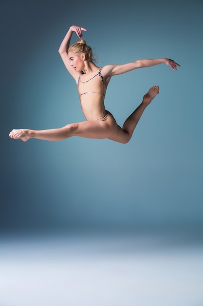 Jeune belle danseuse de style moderne sautant sur un fond bleu studio