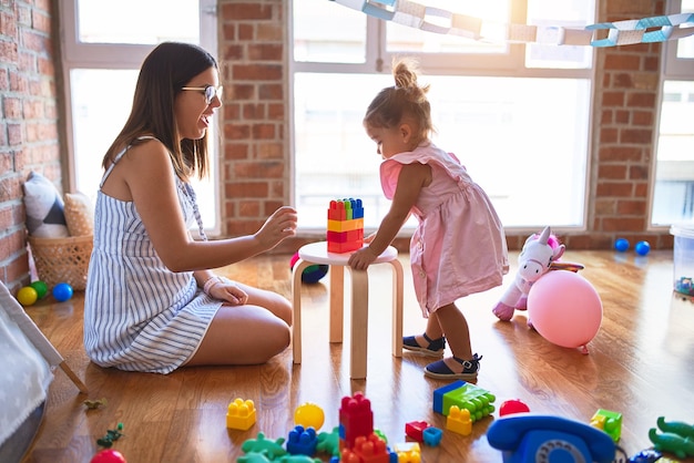 Jeune belle enseignante et enfant en bas âge jouant avec des blocs de construction jouet sur la table à la maternelle