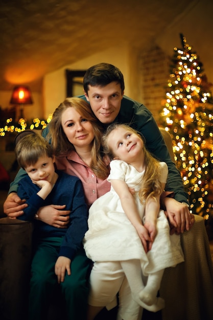 Jeune belle famille avec deux enfants posant sur une chaise dans un intérieur de Noël