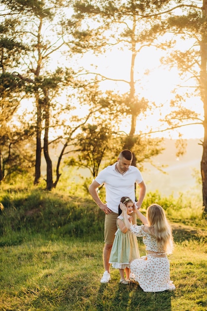 Jeune belle famille avec une petite fille câlin baiser et promenade dans la nature au coucher du soleil Photo d'une famille avec un petit enfant dans la nature
