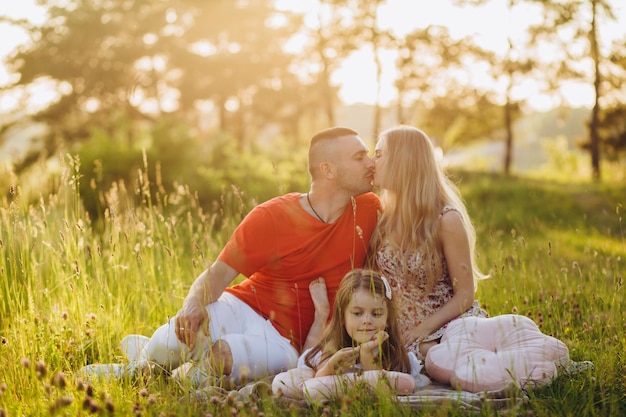 Jeune belle famille avec une petite fille câlin baiser et promenade dans la nature au coucher du soleil Photo d'une famille avec un petit enfant dans la nature