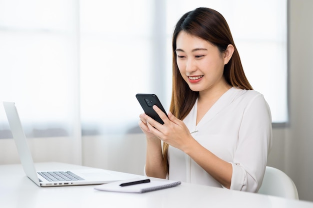 Jeune belle femme d'affaires asiatique à l'aide de smartphone. Souriante charmante jeune femme heureuse textos touchant sur l'écran du téléphone portable.