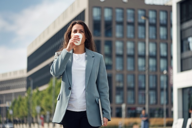 Jeune belle femme d'affaires dans des vêtements décontractés près du centre de bureaux avec une tasse de café pause déjeuner