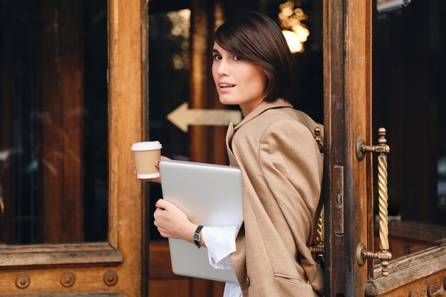 Jeune belle femme d'affaires élégante avec ordinateur portable et café en cours de travail en plein air