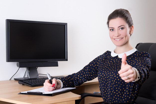 Jeune belle femme d'affaires pouce en l'air au bureau et moniteur pc avec écran vide