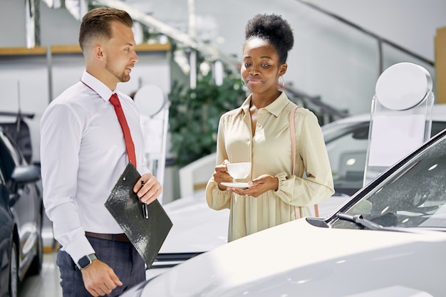 Photo jeune belle femme africaine attrayante boire une tasse de thé et écouter attentivement l'agent de vente professionnel