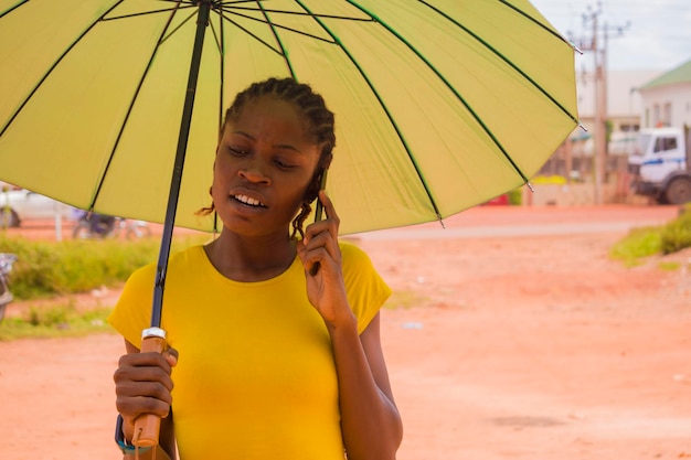 Jeune belle femme africaine utilisant un parapluie pour se protéger sous un temps très ensoleillé et passer des appels avec son téléphone portable