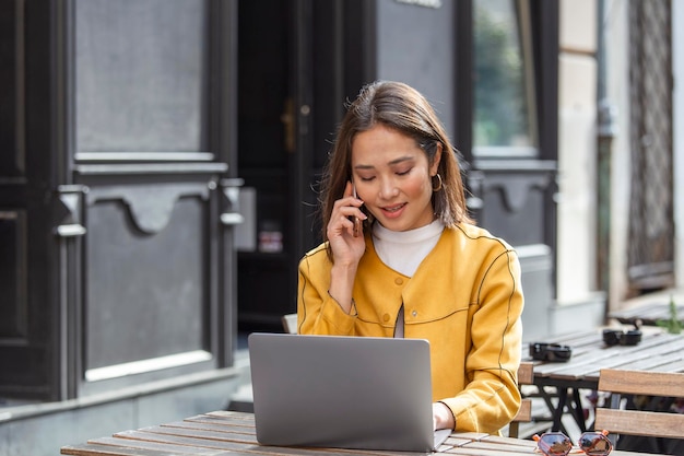 Jeune belle femme asiatique assise dans un café à une table en bois buvant du café et utilisant un ordinateur portable