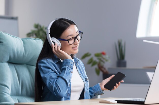 Jeune belle femme asiatique écoutant de la musique au bureau à l'aide d'un téléphone et d'une application musicale femme d'affaires avec un casque au repos