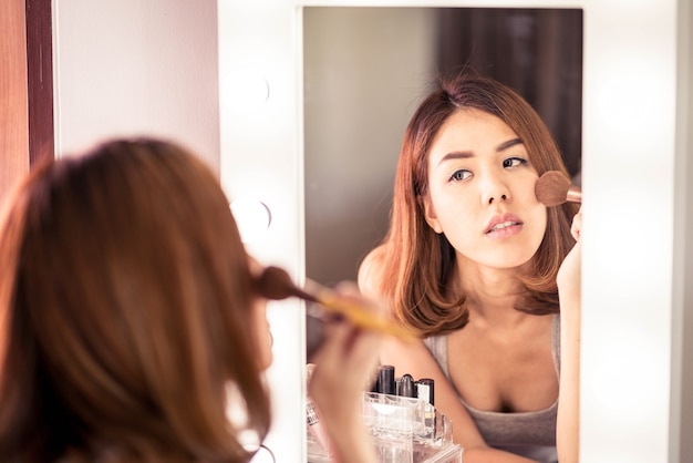 Jeune belle femme asiatique maquillant près d&#39;un miroir