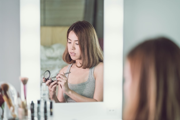 Jeune belle femme asiatique maquillant près d&#39;un miroir