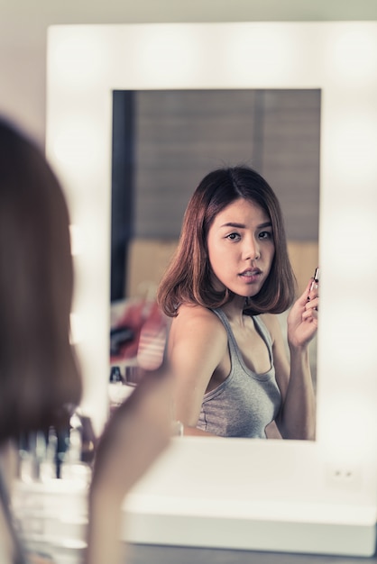 Jeune belle femme asiatique maquillant près d&#39;un miroir