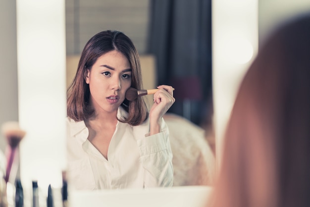 Jeune belle femme asiatique maquillant près d&#39;un miroir