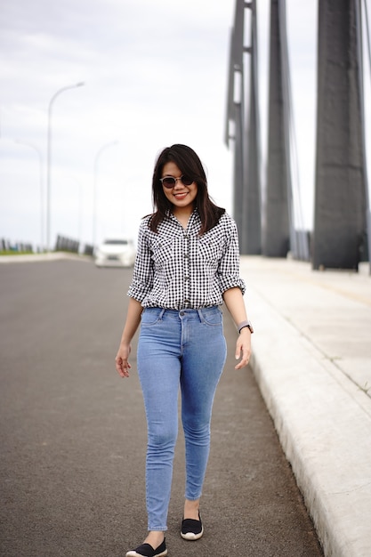 Jeune belle femme asiatique portant une chemise à carreaux et un jean bleu posant à l'extérieur