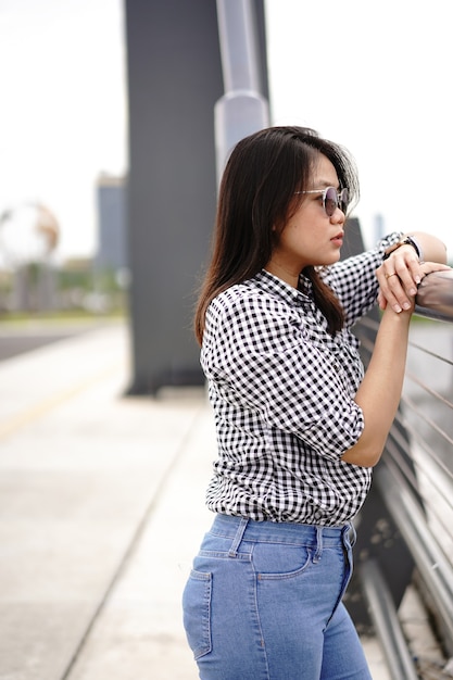 Jeune belle femme asiatique portant une chemise à carreaux et un jean bleu posant à l'extérieur