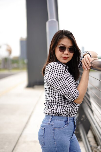 Jeune belle femme asiatique portant une chemise à carreaux et un jean bleu posant à l'extérieur