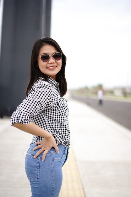 Jeune belle femme asiatique portant une chemise à carreaux et un jean bleu posant à l'extérieur