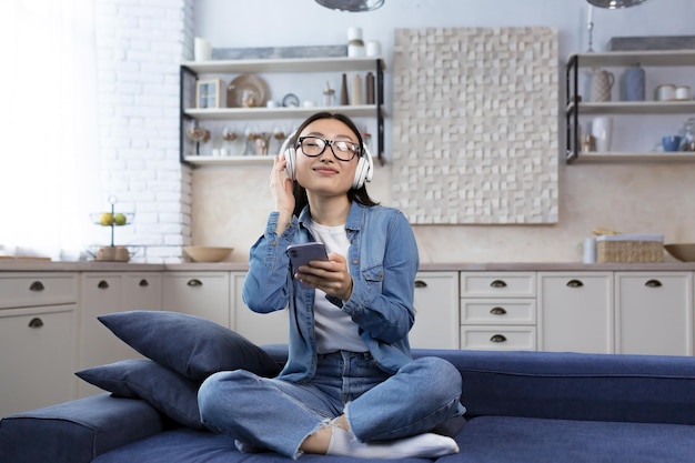 Jeune belle femme asiatique se détendre à la maison assise sur un canapé dans le salon étudiante écoutant