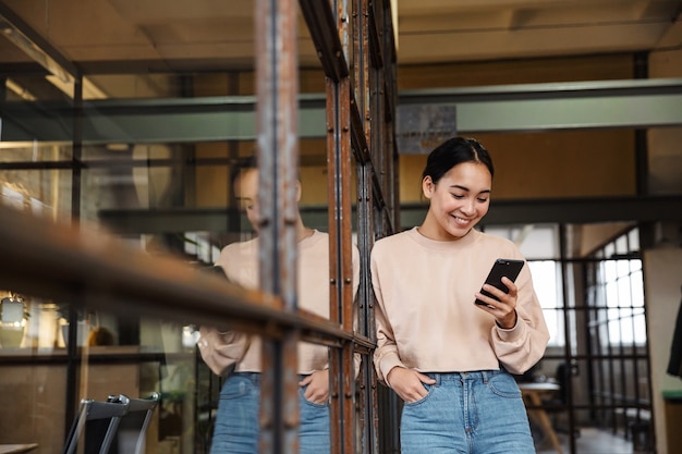 jeune belle femme asiatique souriante et tenant un téléphone portable tout en travaillant au bureau