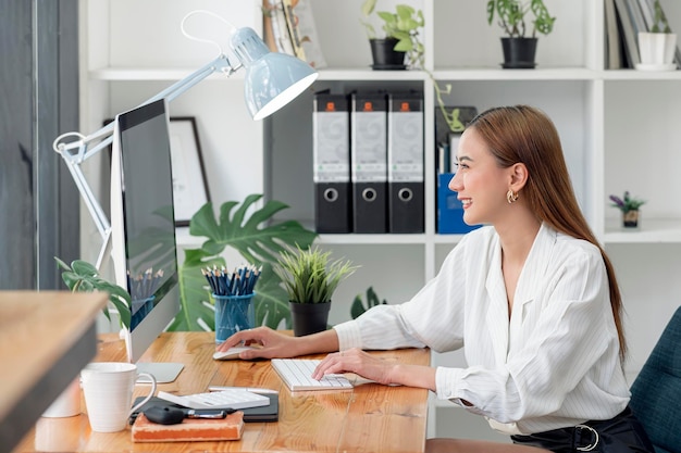 Jeune belle femme asiatique travaillant au bureau, assise au bureau, utilisant un ordinateur de bureau.