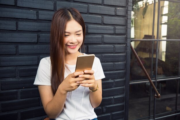 Jeune belle femme asiatique en utilisant son téléphone intelligent pour écouter et regarder de la musique en ligne