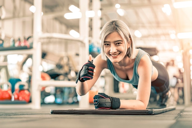 Photo jeune belle femme asiatique en vêtements de sport faisant de l'exercice de planche dans la salle de fitness