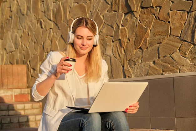 Jeune belle femme au casque avec ordinateur portable, boire du café dans une tasse en papier