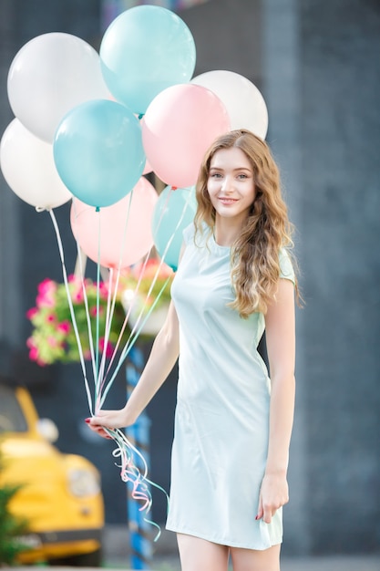 Jeune belle femme avec des ballons multicolores volants dans la ville