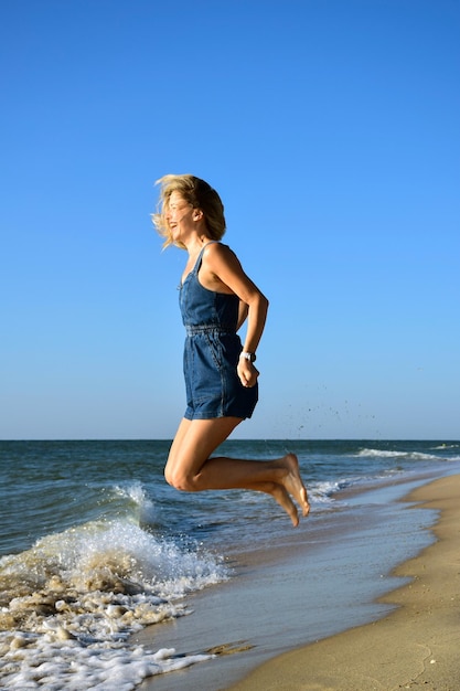 Jeune belle femme blanche blonde sautant sur la plage de la mer et riant