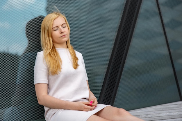 Jeune belle femme blonde assise à l'extérieur sur la terrasse en bois de la ville et se reposant Fille a une pause passer du temps à l'extérieur et se détendre Temps avec soi-même rêvant de relaxation santé mentale