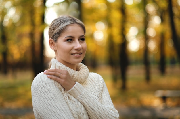 Une jeune belle femme blonde dans un pull blanc se promène dans le parc d'automne