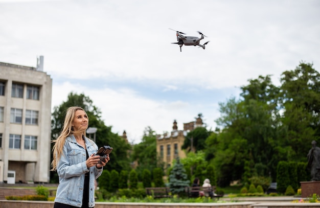 Jeune belle femme blonde pilotant un drone tenant une télécommande à la main