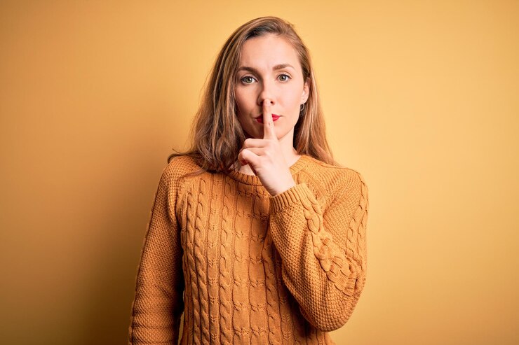 Photo jeune belle femme blonde portant un pull décontracté debout sur fond jaune demandant de se taire avec le doigt sur les lèvres silence et concept secret
