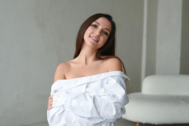 Jeune belle femme brune en chemise blanche portrait élégant et minimaliste avec les épaules nues