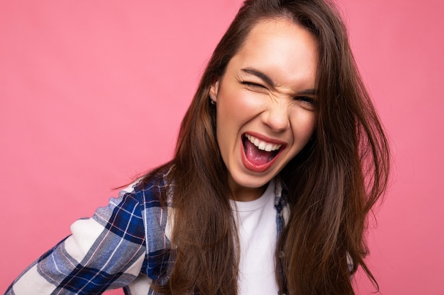 Jeune belle femme brune. Dame à la mode en chemise hipster d'été décontractée. Une femme positive montre des émotions faciales sincères. Modèle drôle isolé sur fond rose avec espace libre.