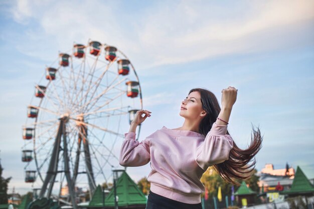 Jeune belle femme brune heureuse dans la ville sur fond de parc et grande roue