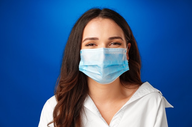 Jeune belle femme brune portant un masque médical sur fond bleu