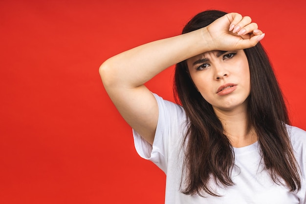 Jeune belle femme brune souffrant de maux de tête désespérés et stressés parce que la douleur et la migraine sont isolées sur fond rouge