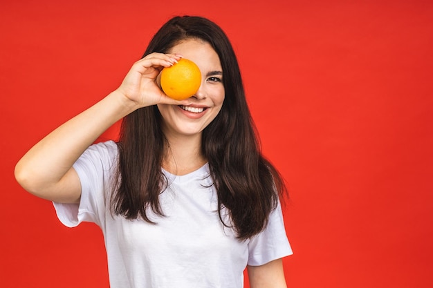 Jeune belle femme brune tenant des fruits orange isolés sur fond rouge