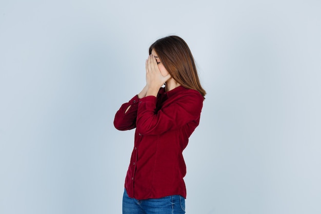 Jeune belle femme en chemise couvrant le visage avec les mains et à la colère