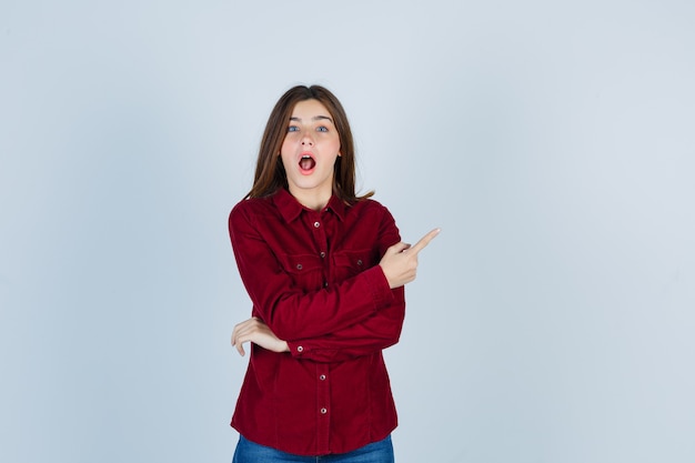 Jeune belle femme en chemise pointant vers le coin supérieur droit et semblant choquée