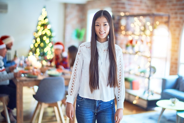 Jeune belle femme chinoise souriante heureuse et confiante debout avec le sourire sur le visage célébrant Noël avec des amis à la maison